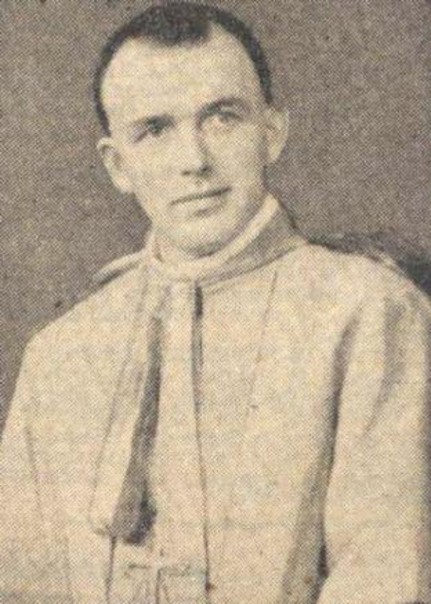 Ein Schwarz-Weiß-Foto eines Mannes in Priesterrobe, der eine weiße Robe mit schwarzem Kragen und Manschetten und einen schwarzen Hut mit einer weißen Feder trägt, mit gefalteten Händen und einem ernsten Gesichtsausdruck.