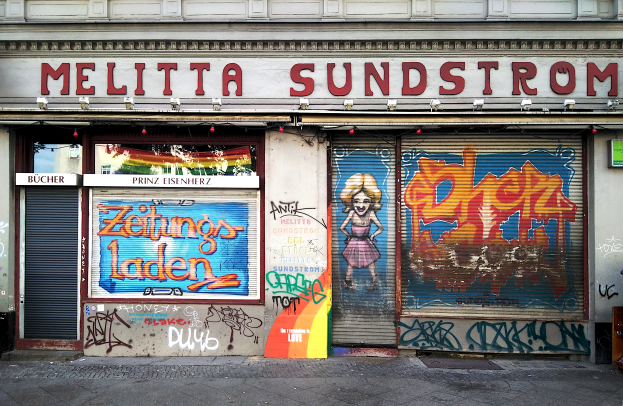 Ein Gebäude mit Graffiti, Rollläden und Schildern mit Text, beleuchtet von Lichtern, mit einer Straße unten.