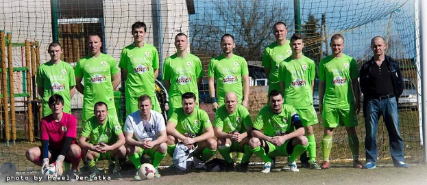 Eine Gruppe von Männern in grünen T-Shirts steht auf einem Fussballfeld, einige sind in der Hocke, mit einem Ball und einem Torpfosten.