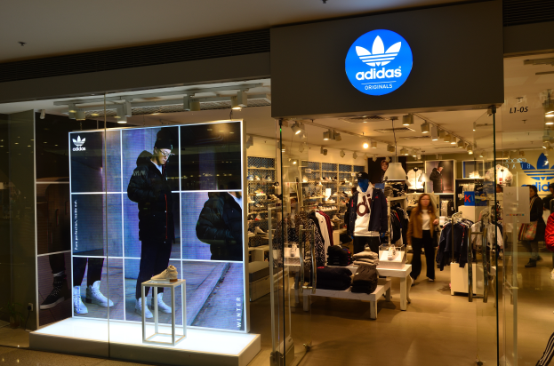 Ein Adidas-Laden in einem Einkaufszentrum mit Schaufensterpuppen, Kleidung, Schuhen und einer Tafel mit dem Adidas-Logo, die darauf hinweist, dass es ein Adidas Originals-Laden ist.
