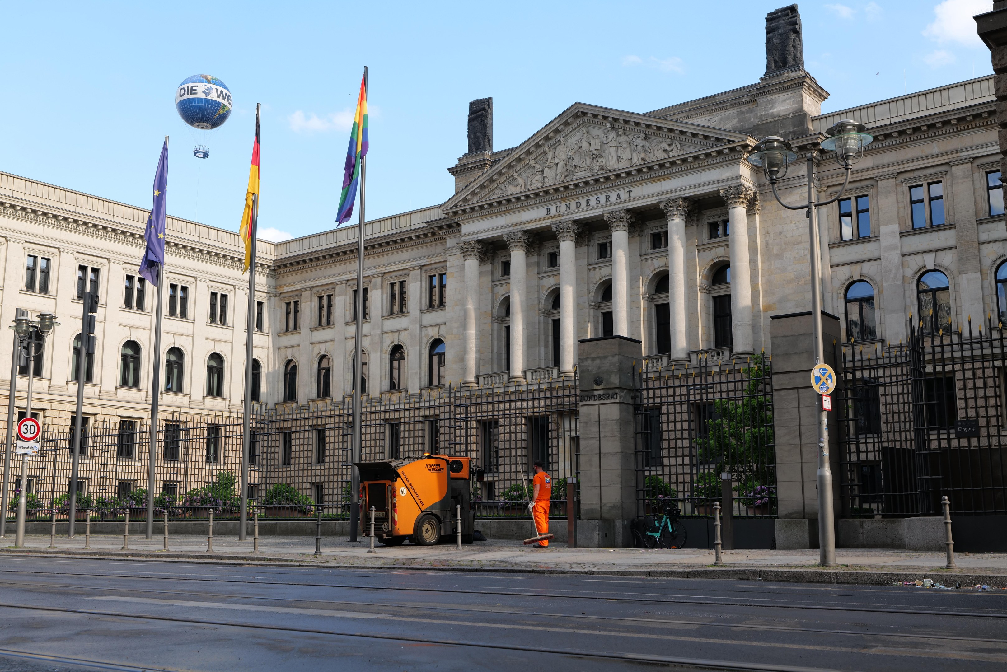 Großes modernes Gebäude mit vielen Fenstern, als Bundestag in Berlin, Deutschland identifiziert, umgeben von Straßeninfrastruktur, Fahrzeugen, Fußgängern und Bäumen unter einem bewölkten Himmel.