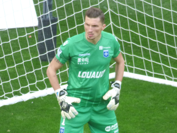 Ein Torwart in grüner Uniform steht vor einem Fußballtor, trägt Handschuhe auf einem Rasenplatz.