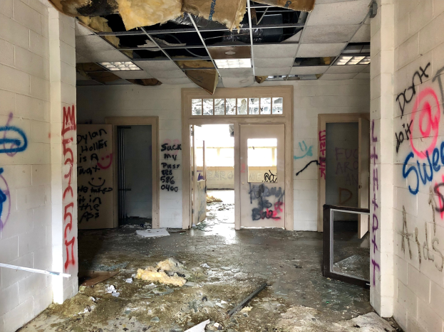 Verlassene Gebäude mit Graffiti-beschmierten Wänden und Decke, Schutt auf dem Boden, mehrere Türen und Fenster im Hintergrund und verstreute Gegenstände.