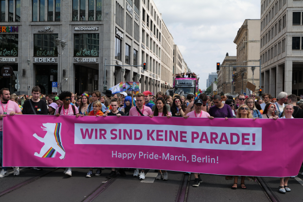 Eine Gruppe von Menschen geht eine Straße in Berlin, Deutschland, entlang und hält eine rosa Schriftzug 'Happy Pride March' mit der Aufschrift 'Happy Pride March'.