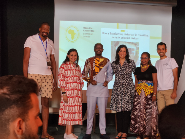 Eine Gruppe von Menschen auf einer Bühne, die lächeln und posieren, mit einem Publikum davor und einem Bildschirm im Hintergrund, der "Open the Knowledge Journalism Awards 2019" anzeigt.