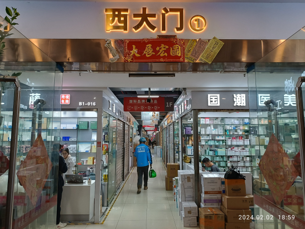 Innenansicht einer chinesischen Apotheke mit Glaswänden, Regalen voller Gegenstände, verstreuten Kartonagen, einer Pflanze auf der linken Seite und einem Namensschild oben, das darauf hinweist, dass es ein chinesischer Drogeriemarkt ist.