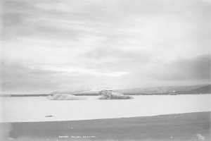 Ein Schwarz-Wei├č-Foto eines Eisbergs, der im Ozean treibt, umgeben von H├Ąngen und einem bew├Âlktem Himmel, mit dem Text "Sunset Childs Glacier" unten.