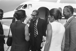 Eine Gruppe von Menschen in Anzügen, die vor einem Flugzeug lächeln, schwarz-weiß.