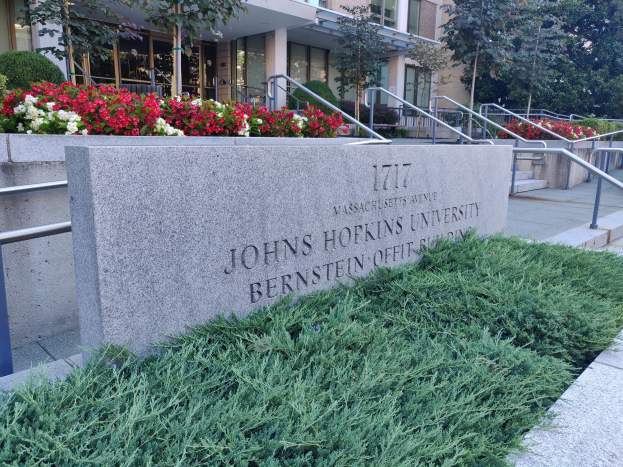 Campus der Johns Hopkins University in Boston, Massachusetts, mit einer Wand mit Text, Geländern, Treppen, Pflanzen, Blumen, Bäumen und einem Gebäude im Hintergrund.