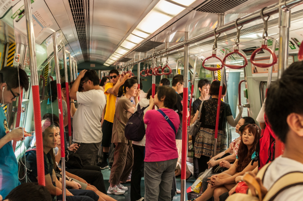 Menschen, die auf einem Zug fahren, einige sitzen auf Sitzen, andere stehen, mit Metallstangen, Griffen und Deckenleuchten im Inneren des Wagens.
