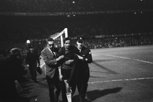 Schwarzes Bild von Fußballspielern, die auf einem Feld mit Torpfosten und einer beleuchteten Zuschauertribüne dahinter feiern.