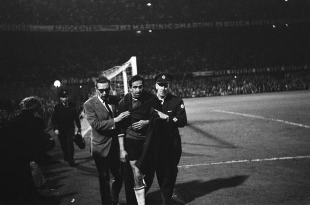 Schwarzes Bild von Fußballspielern, die auf einem Feld mit Torpfosten und einer beleuchteten Zuschauertribüne dahinter feiern.