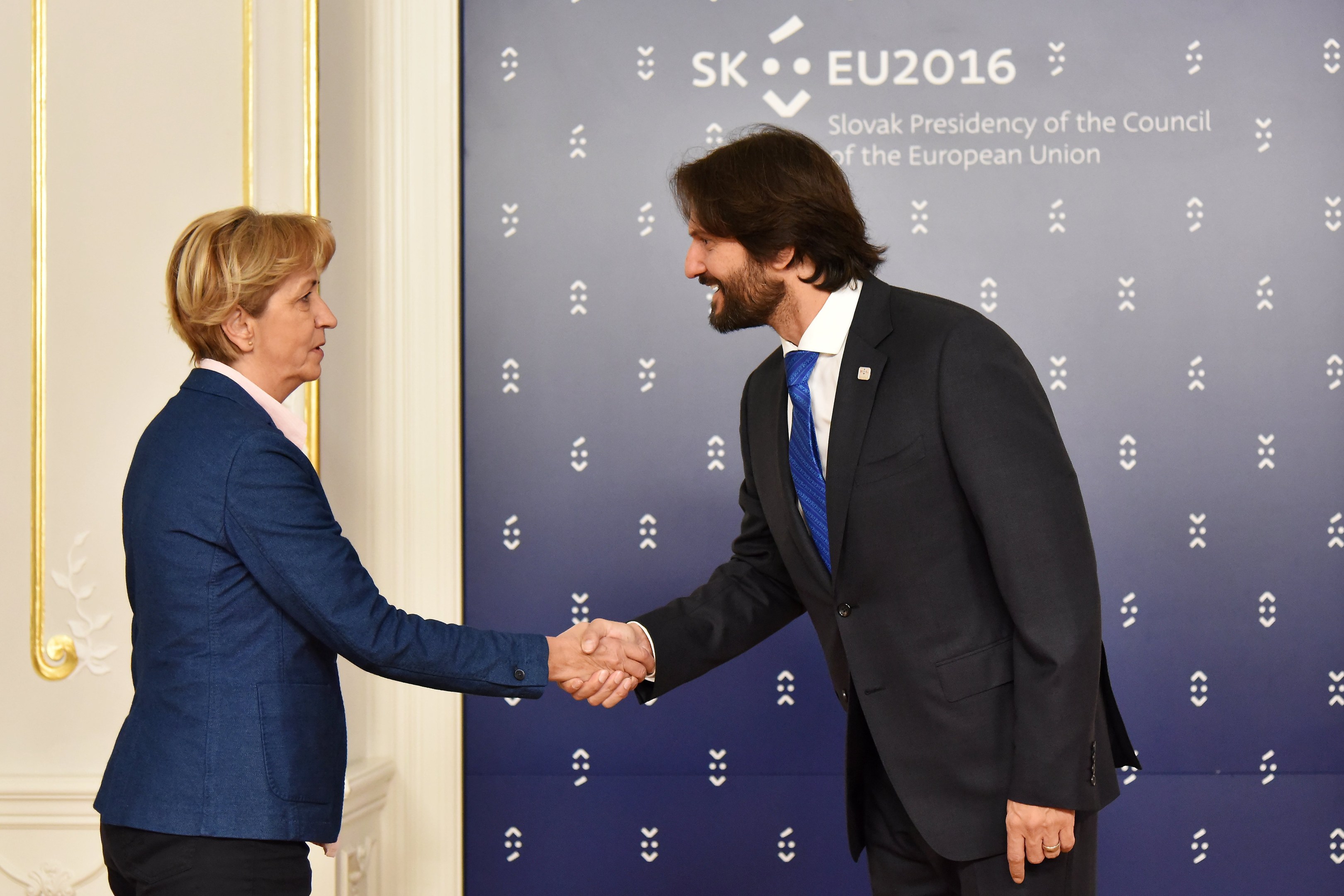 Bundeskanzlerin Angela Merkel und Bundespräsident Joachim Gauck schütteln Hände vor einem "EU-Gipfel"-Plakat, freundlich lächelnd