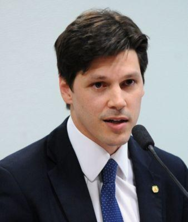 Ein Mann im Anzug und Krawatte spricht vor einer Wand in ein Mikrofon, wahrscheinlich in Reaktion auf eine Regierungserklärung.