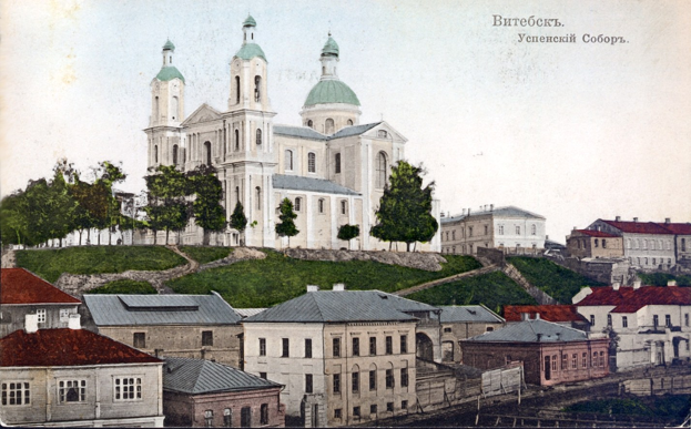 Altes Foto einer Kirche in städtischer Umgebung, umgeben von Gebäuden, Bäumen, Gras und einem klaren blauen Himmel, mit Text oben.