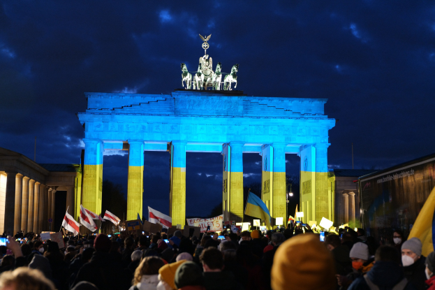 Eine Menschenmenge steht vor dem Brandenburger Tor in Berlin, Deutschland, mit Fahnen, Schildern und einer rechten Banner unter einem bewölkten Himmel.