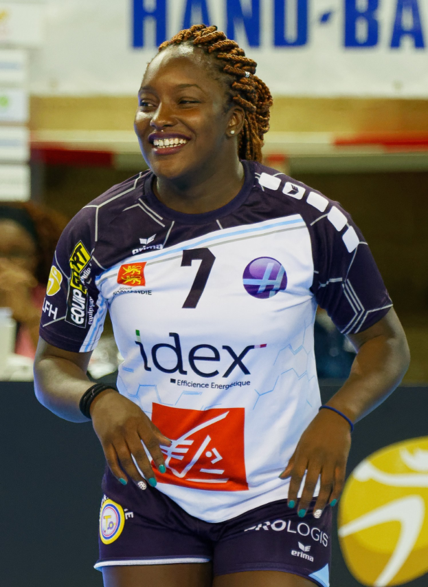 Eine professionelle Handballspielerin in einem lila und weißen Trikot steht lächelnd auf einem Feld während der FIVB-Handball-Weltmeisterschaft 2019.