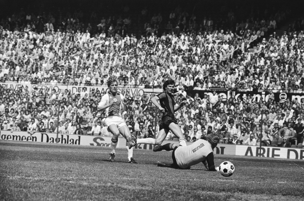 Schwarzes Foto von Männern, die auf einem Feld Füssball spielen, mit Zuschauern im Hintergrund und einem Banner mit der Aufschrift "Bundesliga 1978-79 Ajax 1-1 Hannover 96."