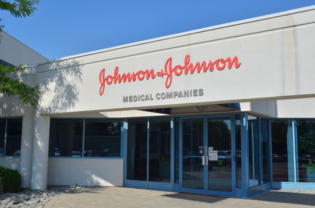 Außenansicht des Johnson & Johnson Medical Companies-Gebäudes mit Glaswänden, Text an der Fassade, Landschaftsgestaltung einschließlich Steinen und einem Baum, unter einem klaren blauen Himmel.