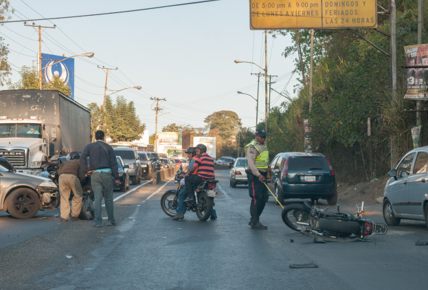 Gruppe von Menschen um ein verunglücktes Motorrad auf dem Seitenstreifen mit mehreren Fahrzeugen, darunter ein Lastwagen, im Hintergrund und Bäumen, Polen, Lampen, Schildern und Himmel.