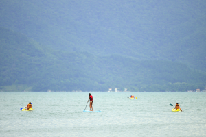 Eine Gruppe von Menschen steht auf dem Wasser mit Paddeln in der Hand, mit Bäumen und Gebäuden im Hintergrund.
