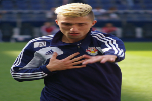 Ein junger Mann in einem blauen T-Shirt steht auf einem Fussballfeld und sieht entschlossen aus, während er als Flügelspieler mit einem unscharfen Hintergrund dargestellt wird.