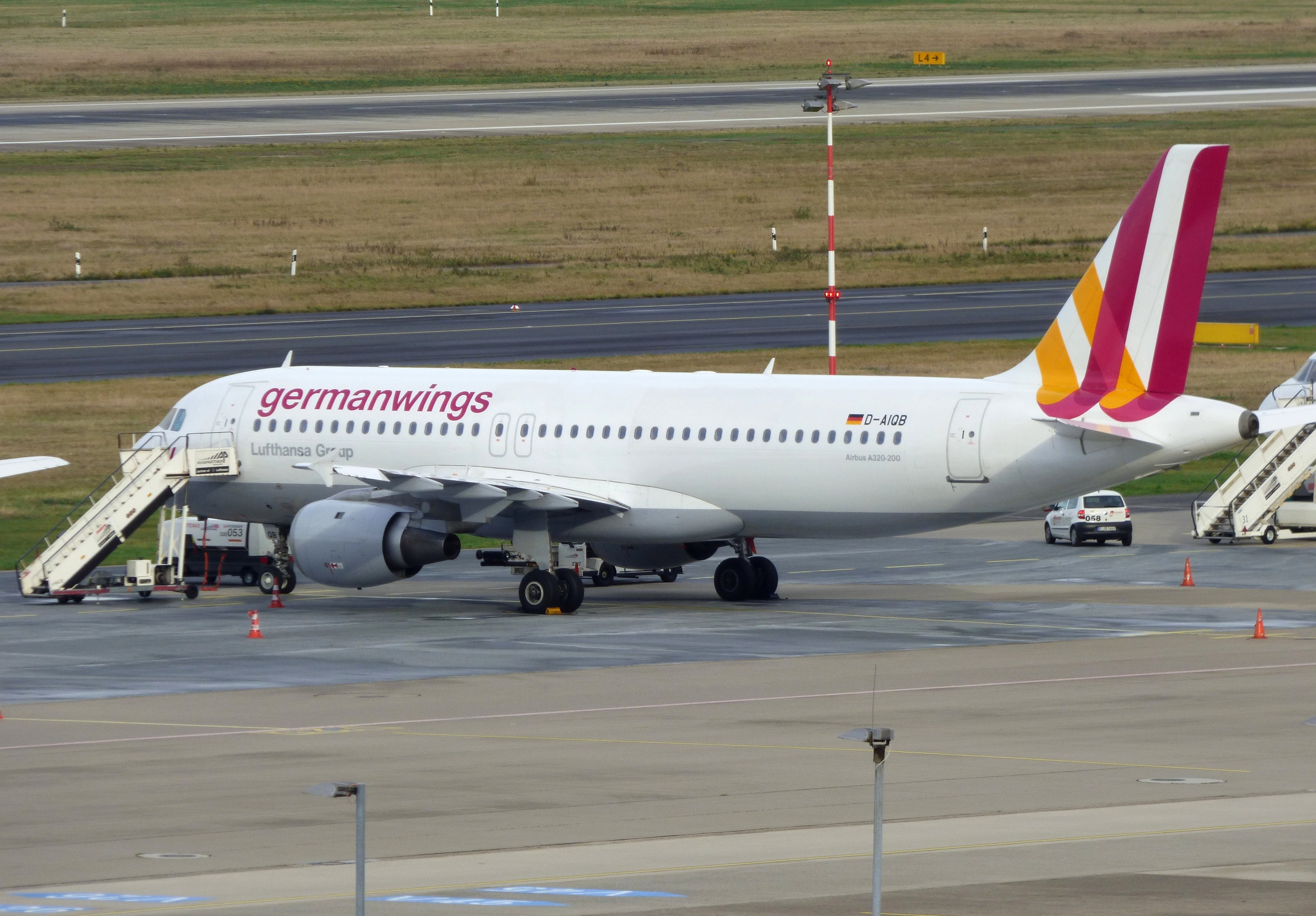 Germanwings Airbus A320-200 geparkt am Frankfurter Flughafen mit Bodenfahrzeugen, Verkehrszeichen, Versorgungsmasten und Grünfläche im Hintergrund.