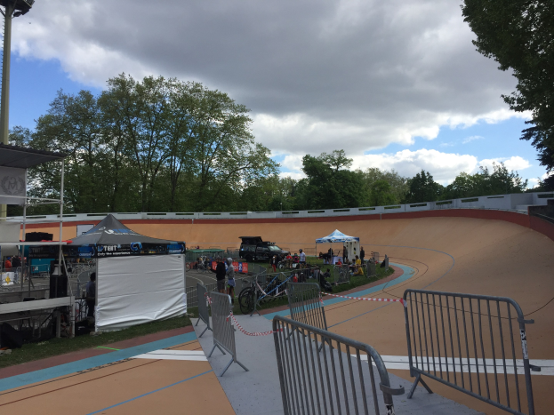 Eine Gruppe von Radfahrern auf einer Schmutzstrecke bei den UCI BMX-Weltmeisterschaften 2018, mit Zelten, Fahrzeugen und Bäumen im Hintergrund.
