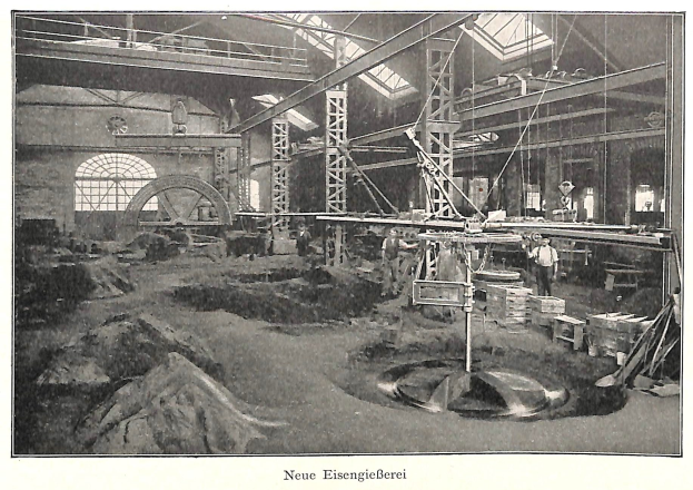 Schwarze und weiße Fotografie eines Fabrikinneren mit Arbeitern, die Maschinen bedienen, Metallstangen und -pole, beschriftet mit "Neue Eisenglebeerei, die erste Fabrik Deutschlands" unten.