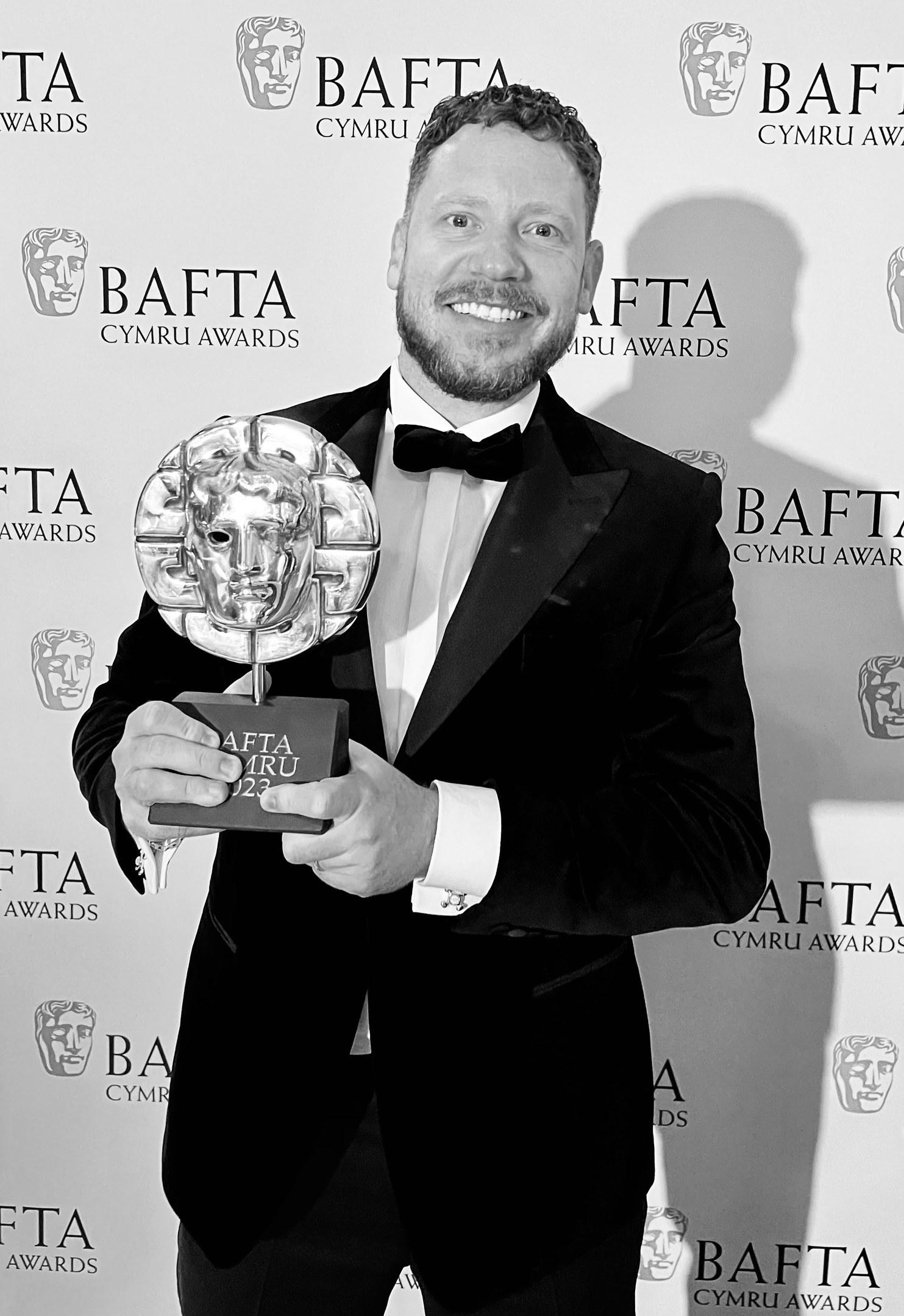 Ein Mann in einem Smoking, der eine BAFTA-Trophäe hält und vor einer Tafel mit der Aufschrift "BAFTA Awards 2018" steht
