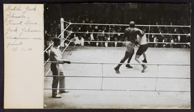 Schwarz-weiß-Foto von zwei Boxern im Ring, ein Schiedsrichter links daneben und Zuschauer im Hintergrund, mit dem Text "Jack Johnson vs Frank Morgan" in der linken oberen Ecke.