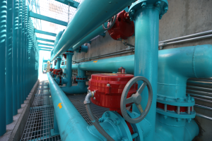 Eine große Gruppe von blauen Rohren und Ventilen in einem Gebäude, mit einem roten Ventil in der Mitte, Metallstangen links und einer Wand im Hintergrund, die wahrscheinlich den Bau einer Gasleitung zeigt.