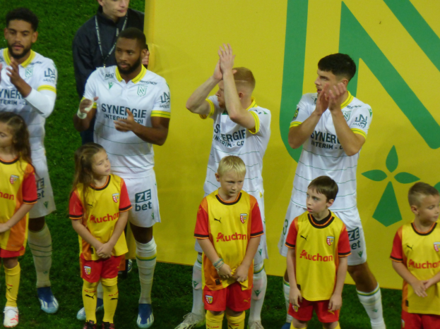 Eine Gruppe von Füßtballspielern in Uniformen klatscht auf einem Ligue-1-Feld in celebration, mit einem "Ligue 1" Schild im Hintergrund.