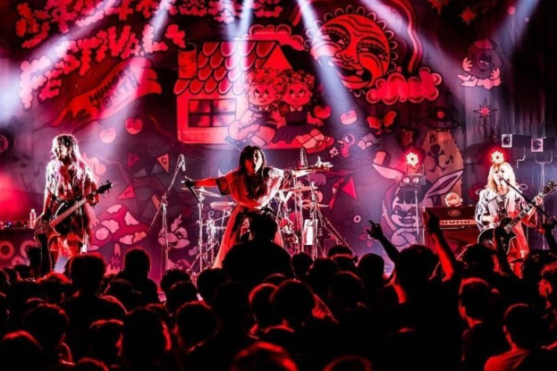 Ein Live-Auftritt der japanischen Rockband Korn, bei dem die Bandmitglieder Gitarren spielen und singen, während das Publikum unten zuschaut.