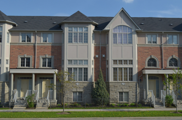 Eine Reihe von Stadthäusern in einer Wohngegend mit sichtbaren Fenstern, Türen, Säulen, Geländern, Stufen, Pflanzen, Bäumen, Gras und Himmel.