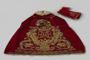 Ein roter Samtmantel mit goldener Stickerei und einer Krone, der mit detaillierten Designs verziert ist, vor einem weißen Hintergrund.