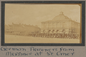Gruppe deutscher Gefangener aus Messines vor einem Gebäude mit einem klaren blauen Himmel im Hintergrund, Text unten sichtbar.