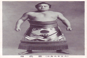 Altes Schwarz-Weiß-Foto eines Sumo-Ringers, der in der Mitte steht, mit japanischer Schrift unten.