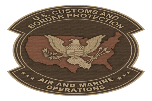 Ein tiefblaues Schild mit einer weißen Umrandung, das ein zentrales Stern, einen Lorbeerkranz und ein Banner mit der Inschrift "Air and Marine" in Fettschrift sowie die Worte "U.S. Customs and Border Protection Air and Marine Operations" darüber zeigt.