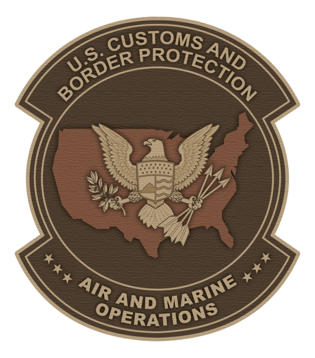 Ein tiefblaues Schild mit einer weißen Umrandung, das ein zentrales Stern, einen Lorbeerkranz und ein Banner mit der Inschrift "Air and Marine" in Fettschrift sowie die Worte "U.S. Customs and Border Protection Air and Marine Operations" darüber zeigt.