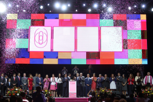 Gruppe von Menschen auf einer Bühne mit einem Podium, Blumensträußen, Kameras und einem großen Bildschirm mit Lichtern für die Eröffnungszeremonie des 2018 China International Film Festivals.