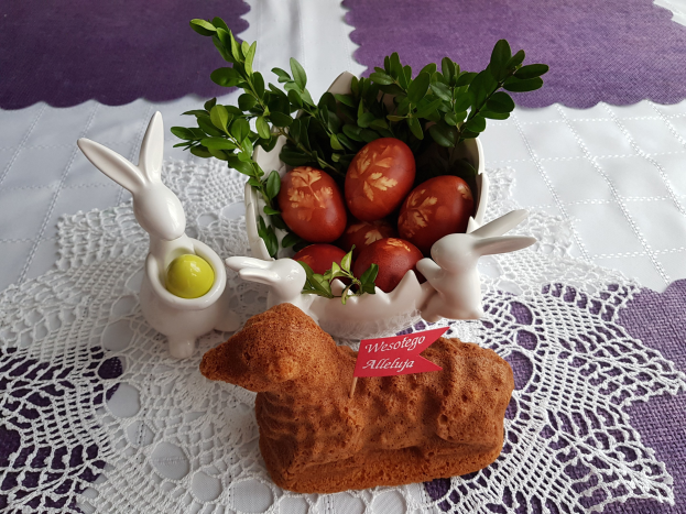 Ein mit einer Decke drapierter Tisch hält eine Schüssel voller bunter Ostereier mit Osterhasenfiguren darauf.