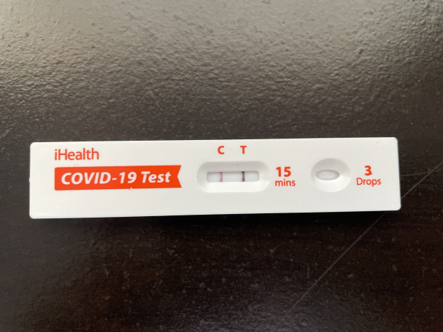 Eine schwarze Oberfläche mit einem weißen und roten Covid-19-Testthermometer, das Text und Zahlen anzeigt.