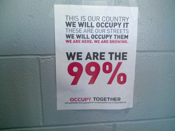 Plakat an einer Wand mit fettem schwarzem Text, der "Occupy Wall Street" und "Wir sind die 99%." lautet.