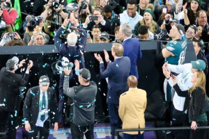 Philadelphia Eagles Spieler feiern mit dem Vince Lombardi Trophy nach dem Sieg im Super Bowl, einige halten den Pokal und andere werfen Konfetti, mit Fotografen und einem Geländer im Hintergrund.