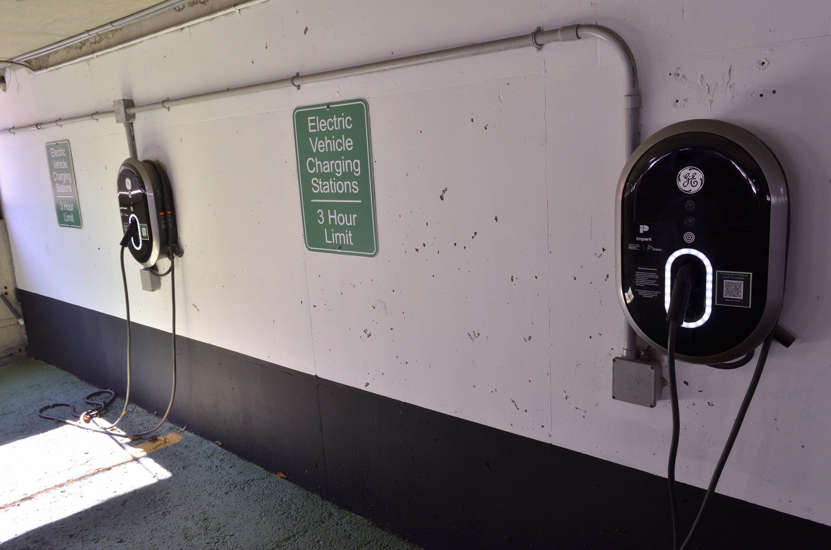 Ladestationen für Elektrofahrzeuge an einer Wand in einer Tiefgarage mit Informationsschildern darüber.