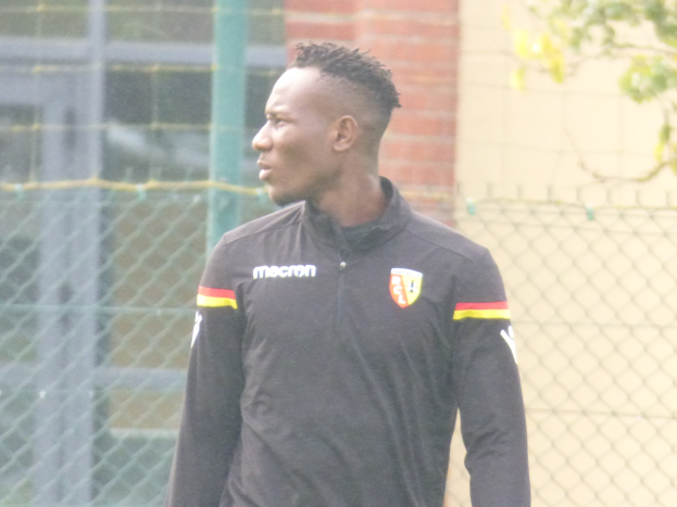 Ein Mann In Einer Schwarzen Jacke Steht Auf Einem Fussballfeld, Umgeben Von Einem Zaun Und Einem Baum, Und Sieht konzentriert Aus During A Training Session.